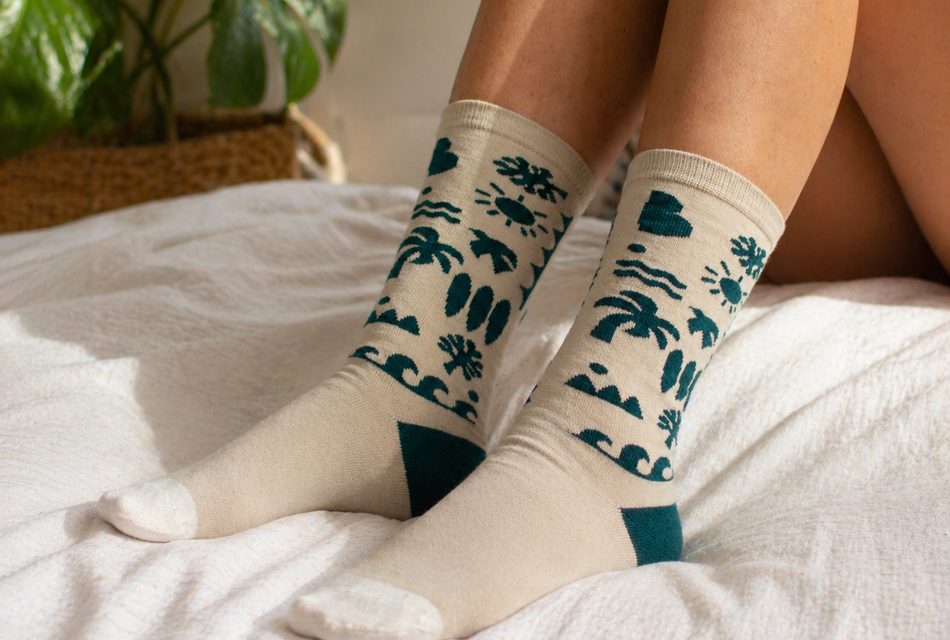 רגליים עם גרבי WildSock בצבע שמנת ודוגמה ירוקה על מיטה, בוקר חורף בבית