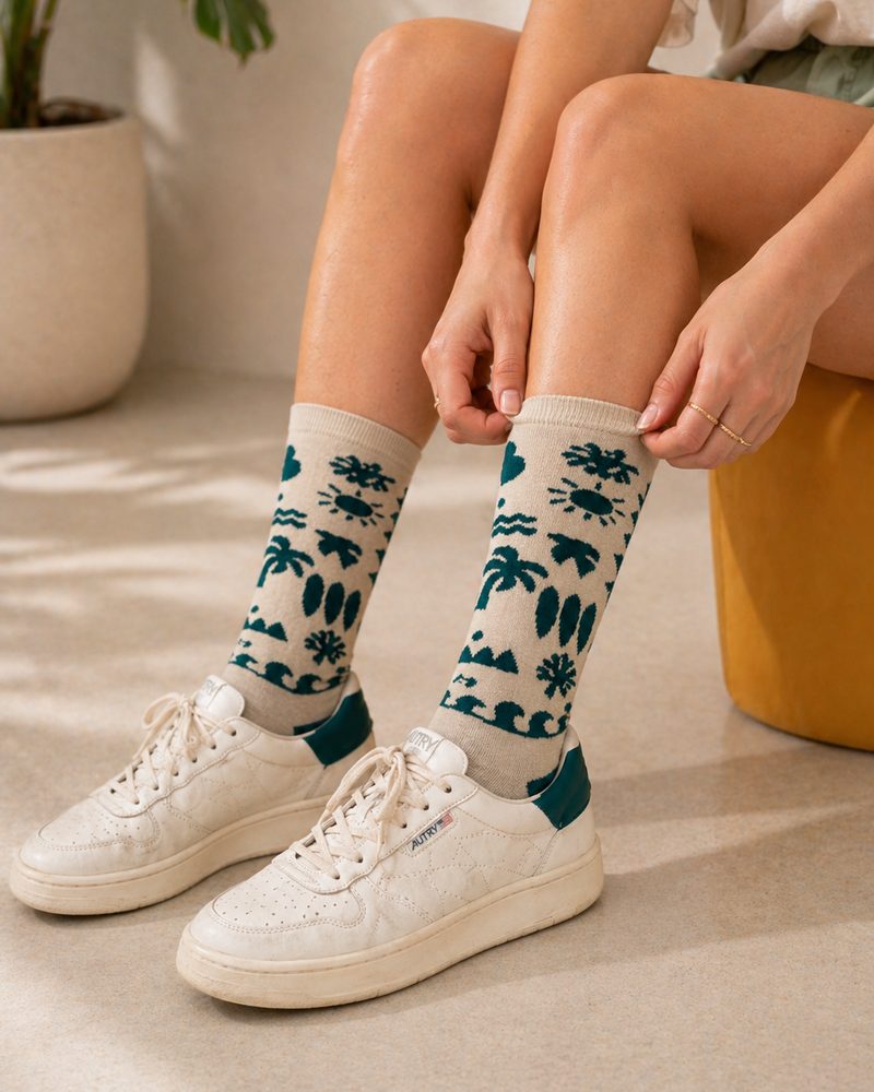 ידיים מסדרות גרבי WildSock בצבע שמנת עם דוגמה ירוקה מעל נעלי סניקרס לבנות