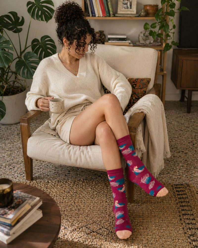 אישה בסוודר לבן יושבת בכורסה בבית עם גרבי WildSock בצבע בורדו